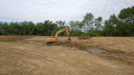 Powerful-hydraulic-excavator-scooping-dirt-from-a-muddy-area-at-the-bottom-of-a-slope-to-a-drier-area-at-a-small-land-development-site