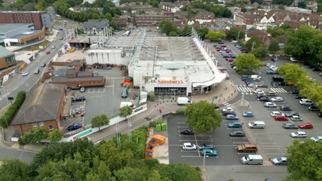 Drohne,-Die-Von-Einem-Supermarkt-Wegfliegt,-Mit-Blick-Auf-Einen-Besiedelten-Parkplatz-Und-Eine-Siedlung-Am-Flussufer