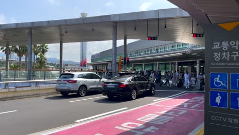 Zeitlupenaufnahme-Eines-Touristenpassagiers,-Der-An-Einem-Sonnigen-Tag-Die-Straße-überquert-Und-Den-Flughafen-Jeju-In-Südkorea-Betritt-–-Totalaufnahme