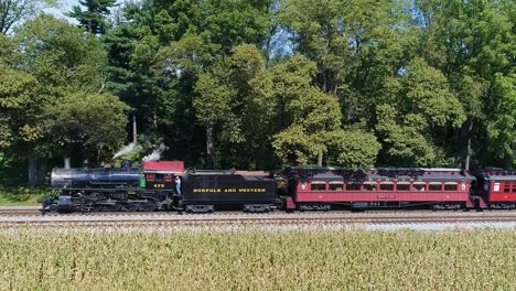 A-Drone-Side-View-of-an-Antique-Steam-Passenger-Train-in-Slow-Motion-Blowing-Smoke-and-Steam-Traveling-Thru-Fertile-Corn-Fields-and-Traveling-Through-Trees-on-a-Sunny-Summer-Day