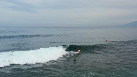 young-man-surfing-a-small-wave-in-Nusa-Ceningan-Bali-on-cloudy-day,-aerial