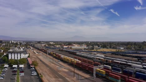 Aerial-descending-close-up-shot-of-a-freight-train-passing-through-the-railyards-of-downtown-Bakersfield,-California