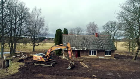 A-drone-captured-an-excavator-tearing-up-the-earth-in-front-of-a-small-cottage-and-a-tractor-hauling-heavy-materials