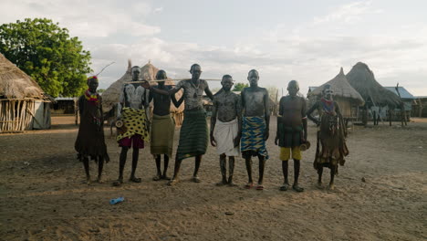 Indigenous-People-Of-Karo-Tribe-With-Body-Paint-Standing-With-Thatched-Houses-In-The-Background-In-Omo-Valley,-Ethiopia