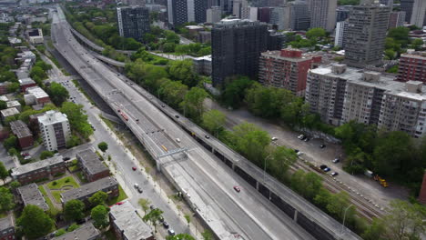 Aerial-View-of-Fluid-Cars-Traffic-on-Suburban-Highway-in-Montreal-Area-Canada,-Modern-Multi-Lanes-Driveway-Road-Infrastructure-Surrounded-by-Residential-Buildings-Towers-and-Homes