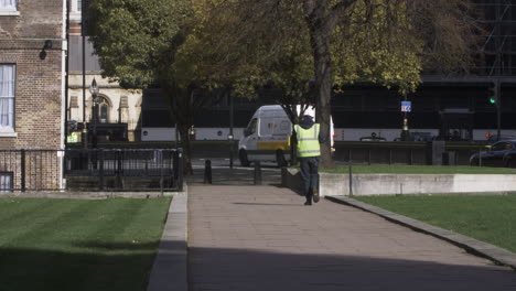 Hombres-Vestidos-Con-Casco-Y-Chaqueta-De-Alta-Visibilidad-Caminando-Por-Los-Jardines-De-La-Calle-Abingdon-En-Westminster