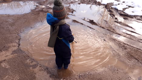 Kid-plays-with-a-wooden-stick-in-a-muddy-puddle-in-winter-and-hitting-the-water-surface