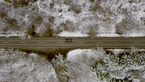 Watching-a-driving-car-from-above-having-a-ride-through-a-winter-landscape-in-a-woodland