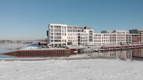 Bright-Noorderhaven-aerial-view-of-contemporary-new-luxury-apartment-building-in-snow-white-cityscape-against-a-clear-blue-sky-reflecting-in-the-IJssel-river-recreational-port-in-the-foreground