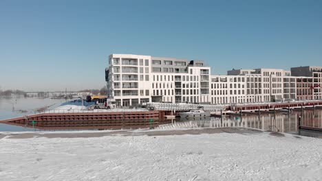 Helle-Noorderhaven-Luftaufnahme-Eines-Modernen-Neuen-Luxusapartmentgebäudes-In-Schneeweißer-Stadtlandschaft-Vor-Einem-Klaren-Blauen-Himmel,-Der-Sich-Im-Freizeithafen-Am-Fluss-Ijssel-Im-Vordergrund-Spiegelt