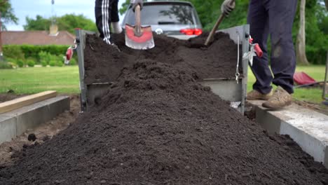 Der-Mutterboden-Wird-Von-Hand-Vom-Autoanhänger-In-Das-Blumenbeet-Im-Garten-Geschaufelt