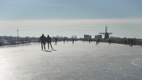 People-ice-skating-on-frozen-Dutch-canals-near-traditional-windmills,-winter