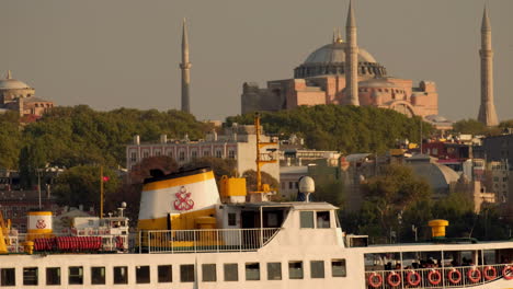 Close-telephoto,-static-clip-of-old-Istanbul-ferry-slowly-passing-the-Hagia-Sophia-at-sunset-in-Istanbul