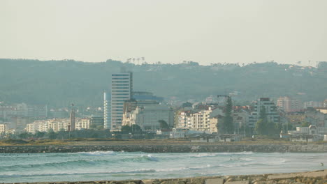 Edificios-Frente-Al-Mar-En-Figueira-Da-Foz,-Portugal-Con-Gente-Nadando-En-El-Agua-Que-Fluye-Del-Río-Mondego-En-Primer-Plano