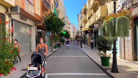 Walking-in-a-typical-Spanish-street-in-old-city-Estepona-with-houses,-restaurants,-businesses-and-people-wearing-face-masks