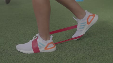Verwendung-Von-Gummibändern-Zum-Training-Mit-Füßen-Auf-Grünem-Gras-Und-Weißen-Tennisschuhen