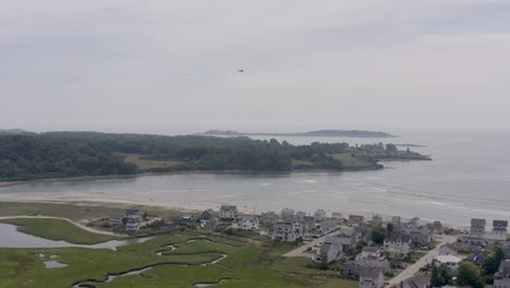 Drone-shot-of-small-Cessna-plane-flying-over-beach-with-people-and-houses-in-Maine