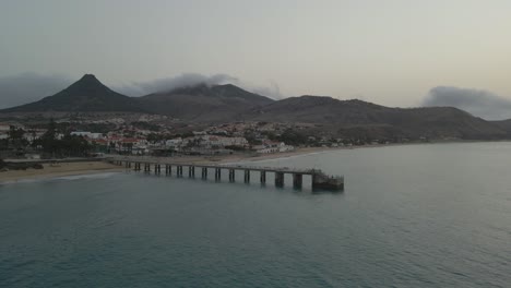 Drone-pans-over-a-pier-as-grey-clouds-roll-over-mountains-in-the-morning