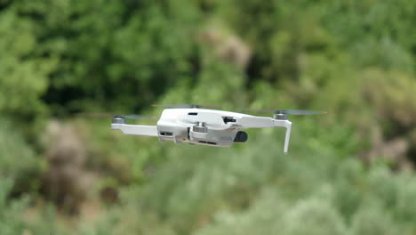 Primer-Plano-De-Un-Dron-Blanco-Flotando-Al-Aire-Libre-Con-Naturaleza-Verde-En-Un-Fondo-Borroso