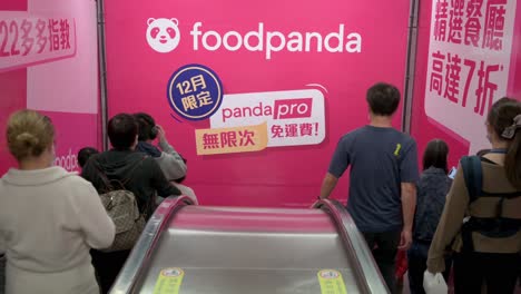 Man-Sieht-Pendler-Auf-Automatischen-Rolltreppen-Fahren,-Während-Sie-In-Einer-U-Bahn-Station-In-Hongkong-An-Einer-Werbung-Des-Multinationalen-Take-Away-Lebensmittelunternehmens-Foodpanda-Oder-Food-Panda-Vorbeifahren