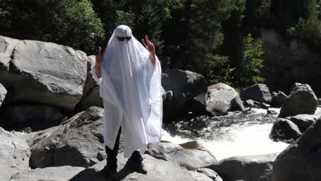 A-dancer-does-trendy-actions-while-wearing-a-ghost-costume-next-to-a-river's-waterfall