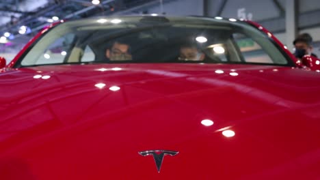 Das-Logo-Von-Tesla-Motor-Ist-Im-Vordergrund-Zu-Sehen,-Wenn-Kunden-Während-Der-International-Motor-Expo-In-Hongkong-Den-Amerikanischen-EV-Elektro-Firmenwagen-Tesla-Model-Y-Testen