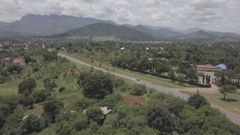 Aerial:-Highway-runs-through-town-in-Malawi-with-mountains-beyond