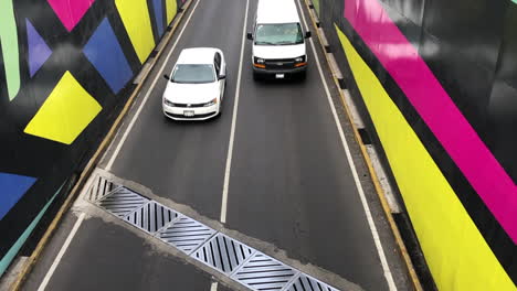 Autos-Moviéndose-En-Una-Carretera-Transitada-Con-Arte-Callejero-Colorido-En-La-Ciudad-De-México