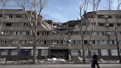 A-man-carrying-a-suitcase-walks-in-front-of-a-hotel-that-was-hit-by-a-cruise-missile,-destroying-a-large-section-of-the-building-during-the-Russian-invasion-of-Ukraine