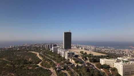 Drone-flight-of-a-high-building-on-the-outskirts-of-a-city-with-a-park-and-nature-trails,-Haifa,-Israel