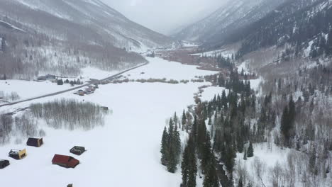 Small-countryside-buildings-surrounded-by-massive-mountain-ranges-in-winter-season,-aerial-drone-view