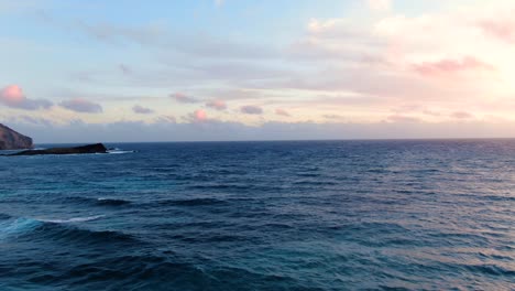 Drone-flying-close-above-the-waves-during-sunrise-with-mini-tropical-islands-in-view