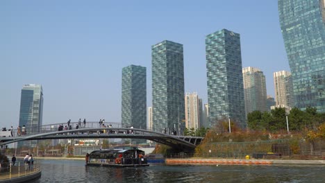 Water-Taxi-Cruise-ship-traveling-on-lake-in-Incheon-Songdo-Central-Park-in-Autumn,-when-people-walking-wearing-face-masks-during-covid-19-pandemic-in-South-Korea