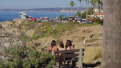 Three-girls-sitting-on-a-bench-taking-a-selfie-in-La-Jolla,-California