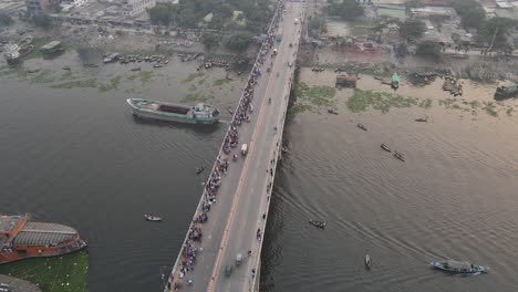 Aerial-view-of-traffic-on-a-bridge-at-Old-Dhaka-steamer-ghat-with-cars-and-ships-crossing-along-Buriganga-river-in-Dhaka,-Bangladesh