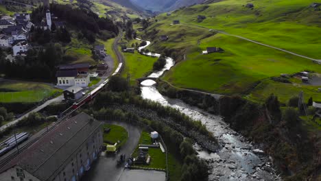 Aerial:-valley,-red-train-leaving-the-town-of-Hospental-in-the-swiss-alps