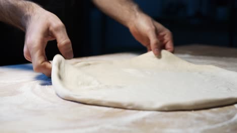A-close-up-of-a-skilled-chef's-hands-put-pizza-dough-on-the-wooden-counter,-shallowing-it-and-set-it-up-for-the-oven