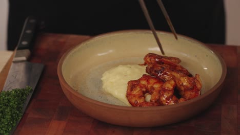 Preparation-of-delicious-shrimp-dish,-professional-chef-slowly-plating-and-placing-shrimps-on-top-of-creamy-mashed-potato-with-tongs