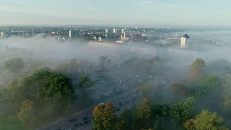 Aerial-backwards-shot-of-mystic-castle-of-Jelgava-and-traffic-on-roads-during-flying-mist-between-city-in-Latvia
