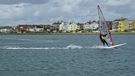 Man-balancing-on-surf-board-in-windy-weather-practicing-windsurfing-skills-on-West-Kirby-marina-lake