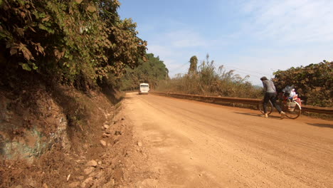 Bus-and-cyclist-going-uphill-in-a-dirt-road-mountain-route,-Vietnam