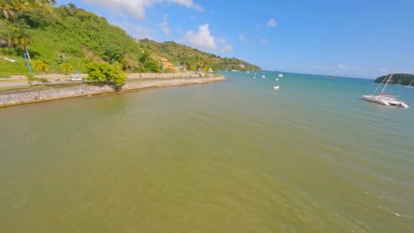 Fpv-flight-along-tropical-coastline-and-bay-of-Samana-Province-with-boats-and-driving-cars-on-road-during-summer
