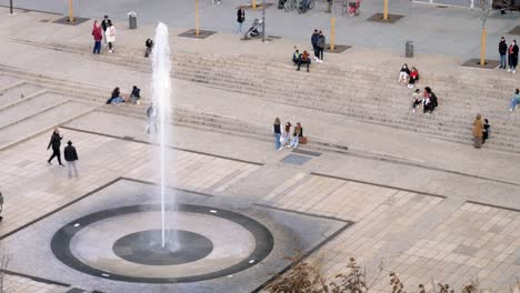 Groups-of-people-sit-on-steps-in-the-town-square-to-watch-a-water-fountain-in-Clermont-Ferrand