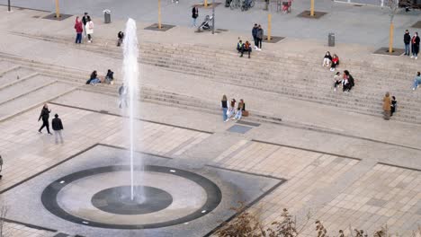 Grupos-De-Personas-Se-Sientan-En-Los-Escalones-De-La-Plaza-Del-Pueblo-Para-Ver-Una-Fuente-De-Agua-En-Clermont-ferrand