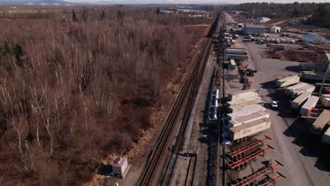 Drone-flying-over-cargo-train-passing-close-to-industrial-zone,-Vancouver-in-Canada