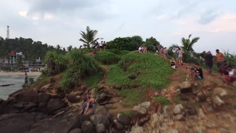 Aufnahme-Von-Menschen,-Die-Auf-Einem-Felsigen-Hügel-Sitzen-Und-Spazieren-Gehen-Und-Einen-Atemberaubenden-Blick-Auf-Den-Goldenen-Sandstrand-Von-Mirissa-In-Sri-Lanka-Genießen