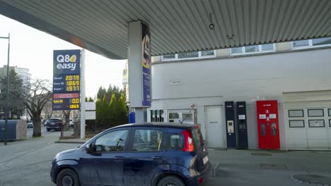 Kleinwagen,-Der-An-Der-Q8-Easy-Tankstelle-Ankommt,-Vor-Einem-Großen-Interaktiven-Schild-Mit-Den-Bisher-Höchsten-Kraftstoffpreisen