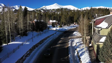 Aerial-forward-view-of-a-mountain-road-with-passing-cars-and-snow-capped-mountains