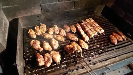 Male-hand-with-thongs-rotating-and-arranging-chicken-wings-grilling-on-a-hot-charcoal-barbecue