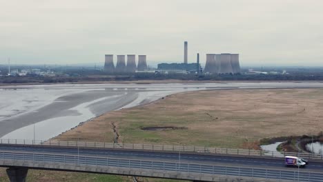 Vehicles-travelling-Mersey-Gateway-bridge-with-Fiddlers-Ferry-power-station-on-river-skyline-aerial-view-pan-right